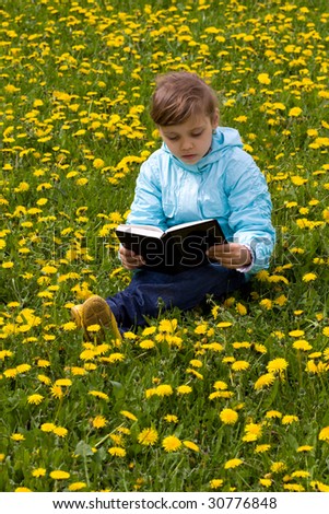 Little caucasian girl on the grass with yellow flowers reading book