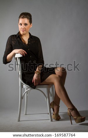 Portrait of sexy woman posing on grey background in studio on chair