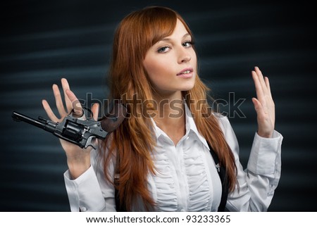 Beautiful girl with red hair gives a revolver. The lifted hands, looks in the camera
