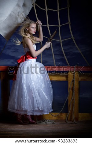 Beautiful girl in a white dress on a deck of the sailing ship with a pistol in hands