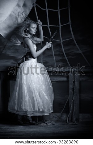 Beautiful girl in a white dress on a deck of the sailing ship with a pistol in hands. Blue toning.