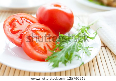 Ripe tomato on a white plate and salad leaves, closeup