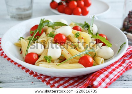 Pasta with vegetables and slices of mozzarella cheese in a plate on napkin, italian food