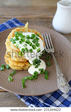 Potato pancakes with sour cream and green onions on a plate, on wooden boards