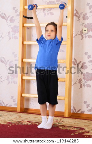 The preschool child lifts dumbbells in a home sports hall