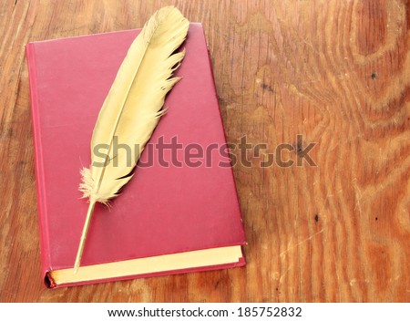 Gold quill pen and red book on grunge wood board