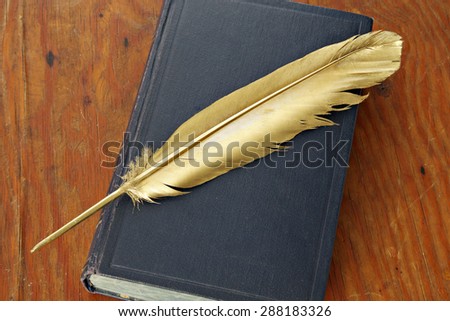 Gold quill pen and antiquarian book on grunge wood board
