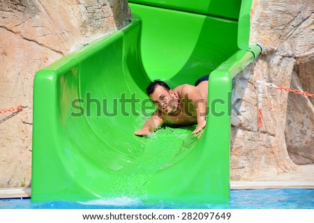 Young man riding down a yellow water slide .Man enjoying a water tube ride