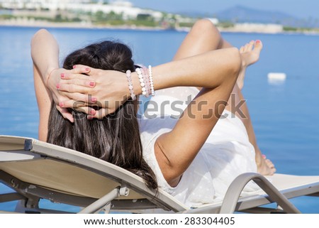 brunette woman with white dress lying on a sunbed and watching the sea landscape