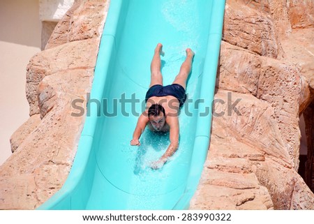 Young man riding down a yellow water slide .Man enjoying a water tube ride