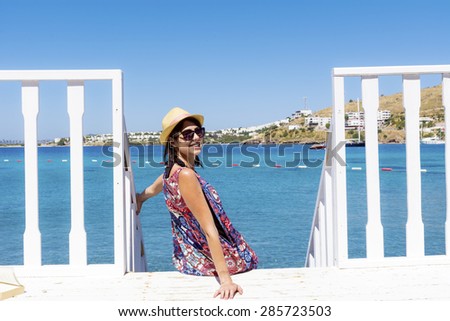 Portrait of  young woman with straw hat sitting on a wooden stairs and watching the sea