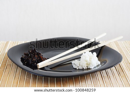 Black dish with white and black rise on a bamboo table cloth still life