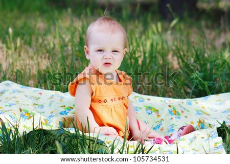 Beautiful little girl in orange dress sitting on a meadow