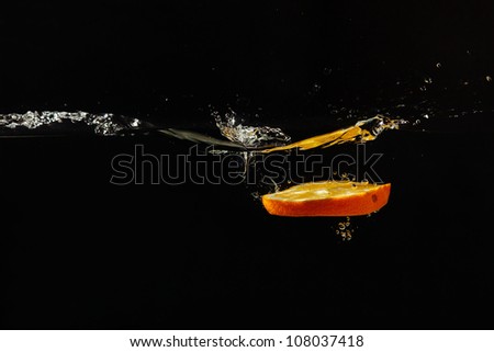 Sliced fresh orange falling into the water with a splash on a black background closeup