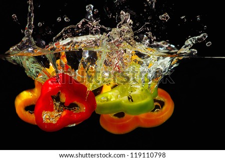 Slices of ripe red, green and yellow pepper falling into the water with a splash on black background