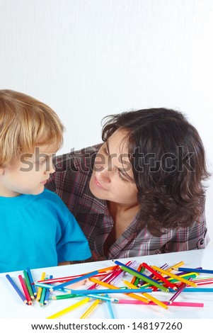 Little boy with his mother draws with color pencils on a white background