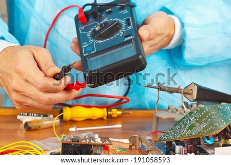 Serviceman checks board of electronic device with a multimeter in the service workshop
