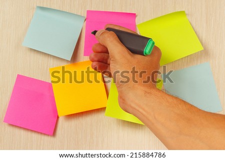 Hand writes a green marker on the sticker on the wooden noticeboard