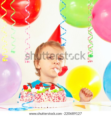 Little boy in festive hat with a birthday cake with whistle and holiday balloons