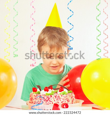 Little blonde boy in holiday hat looking at the birthday cake