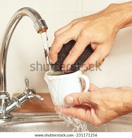 Hands with sponge wash the cup under running water in the kitchen
