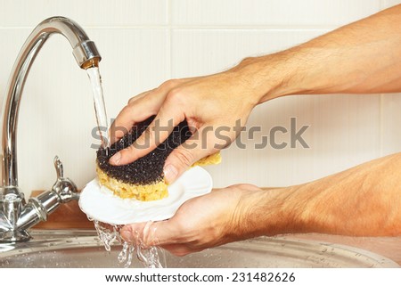 Hands with sponge wash the dirty plate under running water in the kitchen