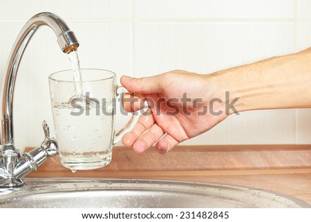 Hands pour water into the glass under the tap in the kitchen