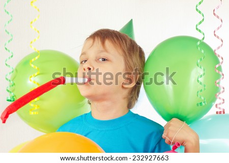 Little boy in festive hat with whistle and holiday balloons and a streamer