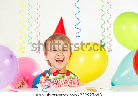 Little blonde boy in holiday hat with a birthday cake and balloons