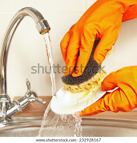 Hands in gloves with sponge wash the plate under running water in the kitchen