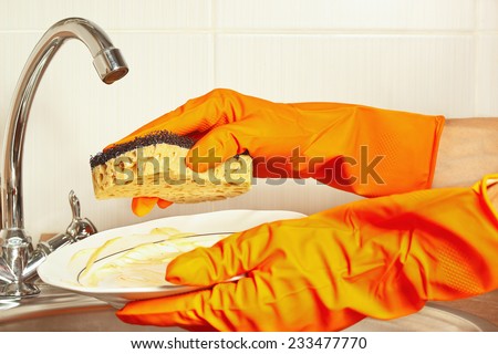 Hands in gloves with dirty plate over the sink in the kitchen