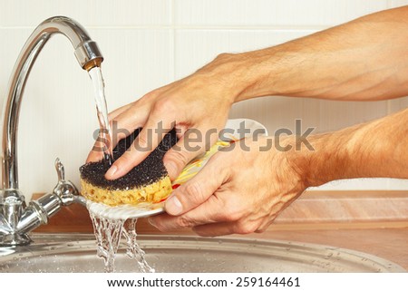 Hands wash the dirty dishes under running water in the kitchen