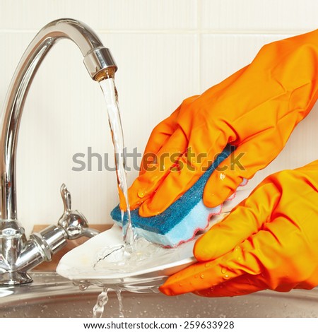 Hands in gloves with sponge wash the dishes under running water in the kitchen