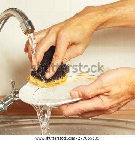 Hands wash the dirty plate under running water in the kitchen