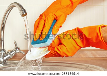 Hands in rubber gloves wash the dishes under running water in the kitchen