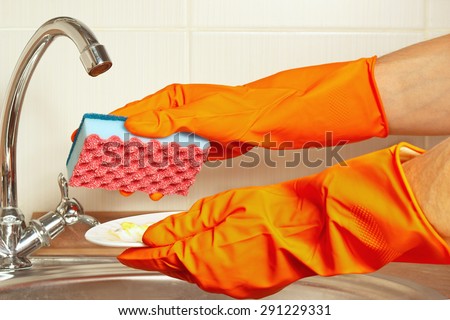 Hands in gloves with sponge and dirty plate over the sink in the kitchen