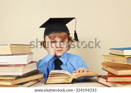 Little tired boy in academic hat studies an old books