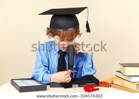 Little professor in academic hat looking through a microscope at his desk