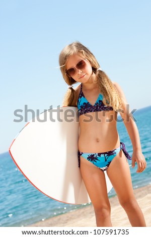 Portrait of cute girl in bikini holding white surfboard on beach.