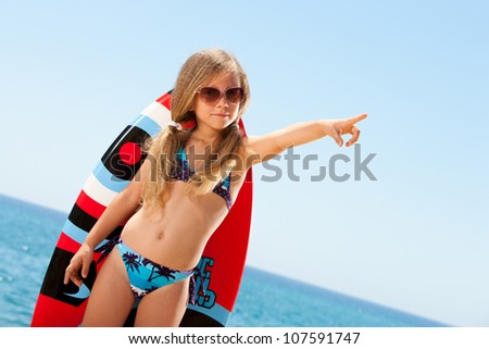 Cute girl in bikini pointing with finger on beach.