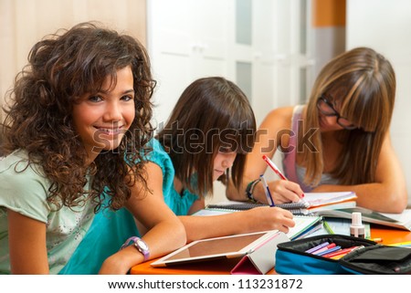 Portrait of cute teenage student doing homework with friends at home.