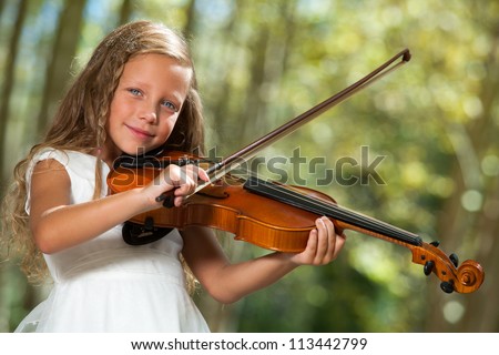Close up portrait of cute girl in white playing violin outdoors.