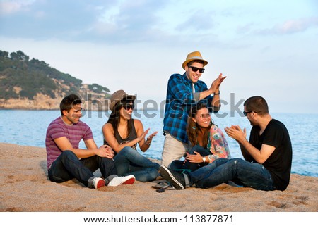 Group of young friends singing and clapping hands on beach.