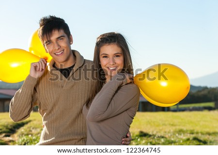 Close up portrait of cute teen couple outdoors with yellow balloons.