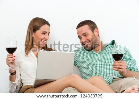 Portrait of couple relaxing with red wine and laptop on couch.