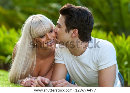 Close up portrait of young man kissing his girlfriend on cheek outdoors.