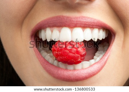 Macro close up of healthy female teeth biting raspberry.