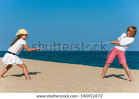 Two kids having a tug war on the beach.