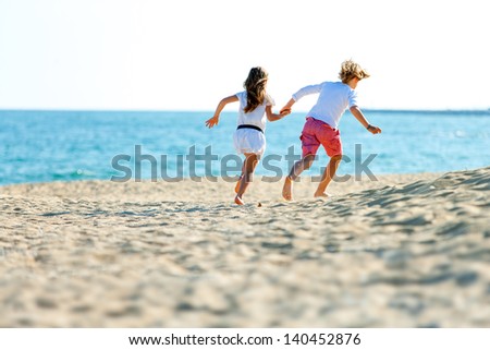 Two kids holding hands running away on sandy beach.