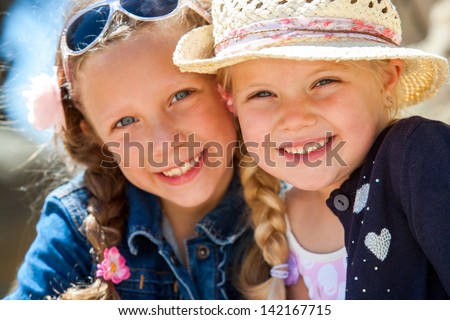 Close up face shot of two young girlfriends smiling with heads together outdoors.